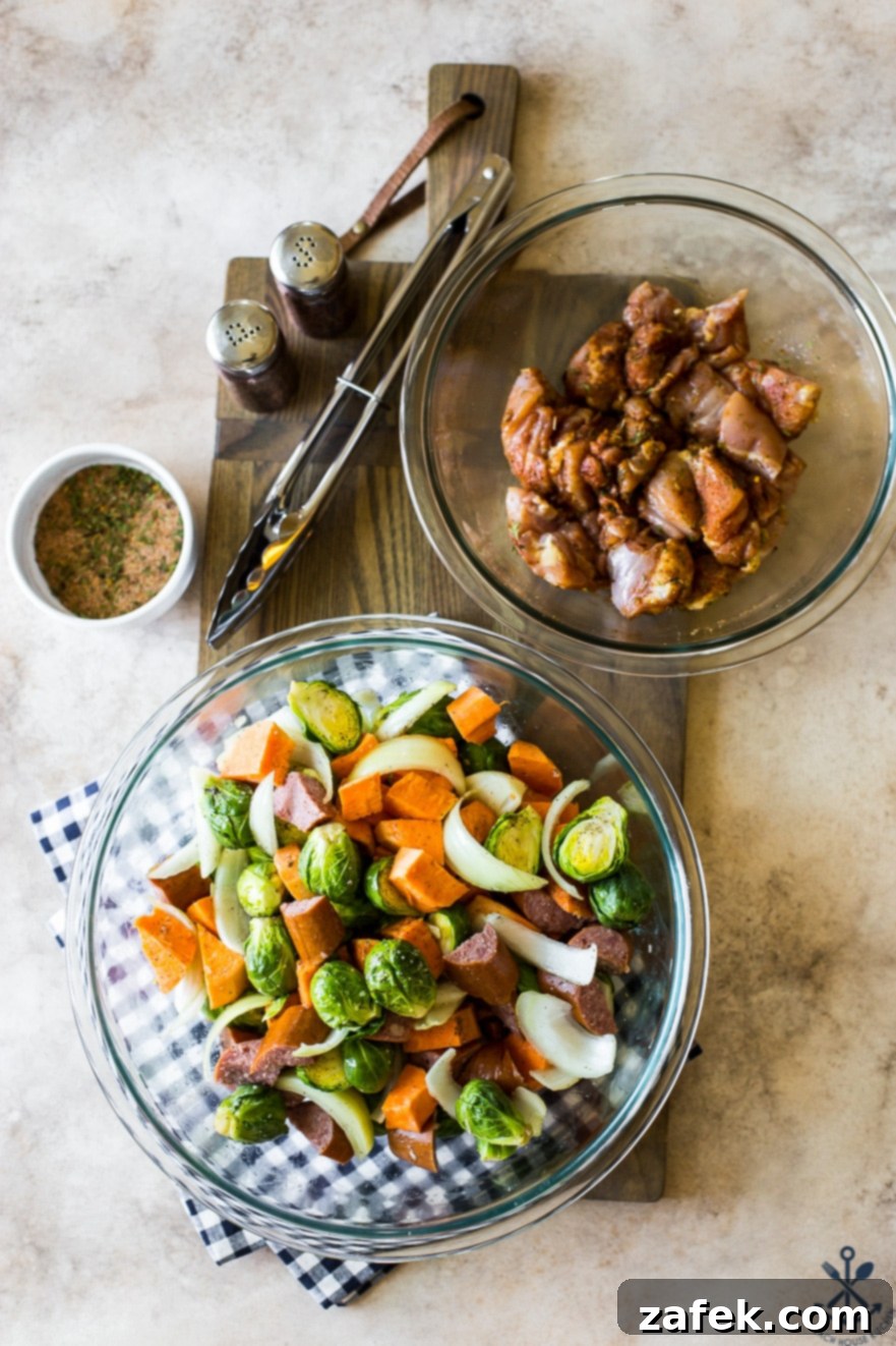 Overhead photo of a bowl of fresh, colorful chopped vegetables and a separate bowl of uncooked chicken chunks, ready for seasoning