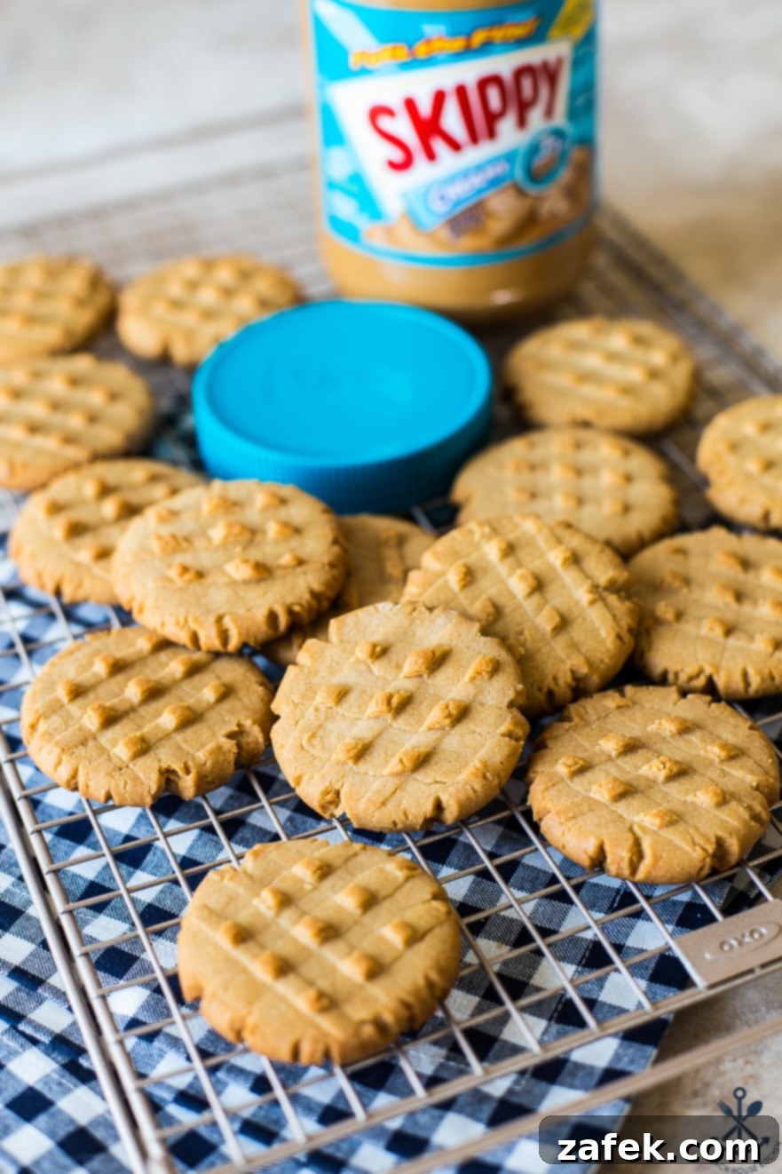Peanut butter cookies on a wire rack with a jar of Skippy peanut butter and a blue lid