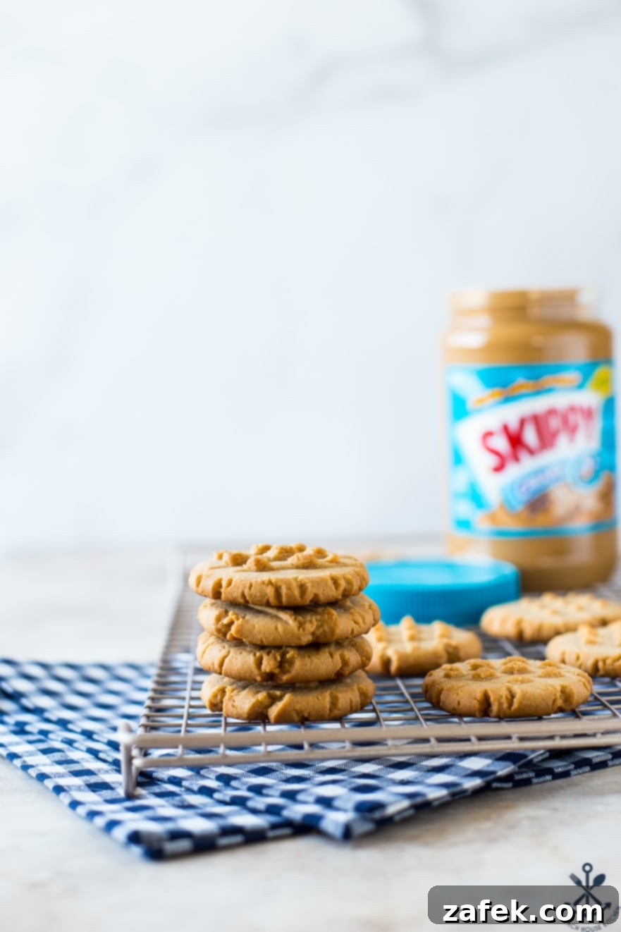 A stack of 4 peanut butter cookies on a wire rack with a jar of peanut butter in the background