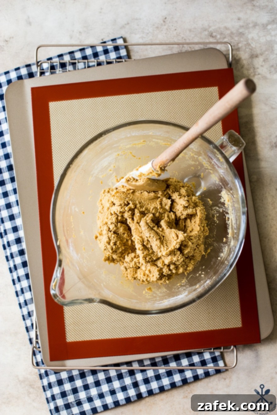 Overhead photo of bowl filled with peanut butter cookie dough on a silpat lined baking sheet on a blue and white checked napkin
