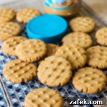 Peanut butter cookies on a wire rack with a jar of Skippy peanut butter and a blue lid