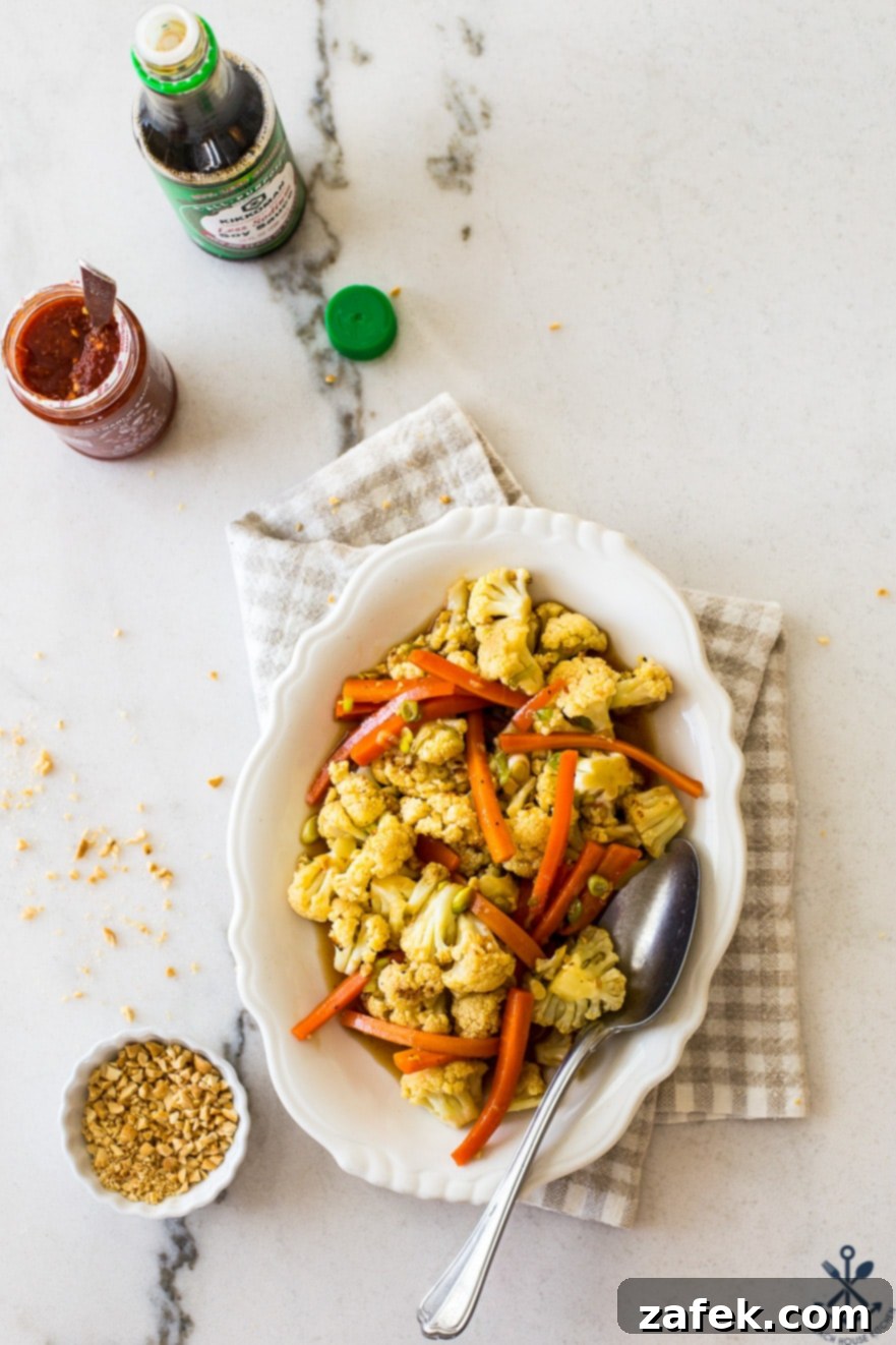 Overhead photo of roasted cauliflower and carrots on a white oval plate, garnished with green onions and peanuts