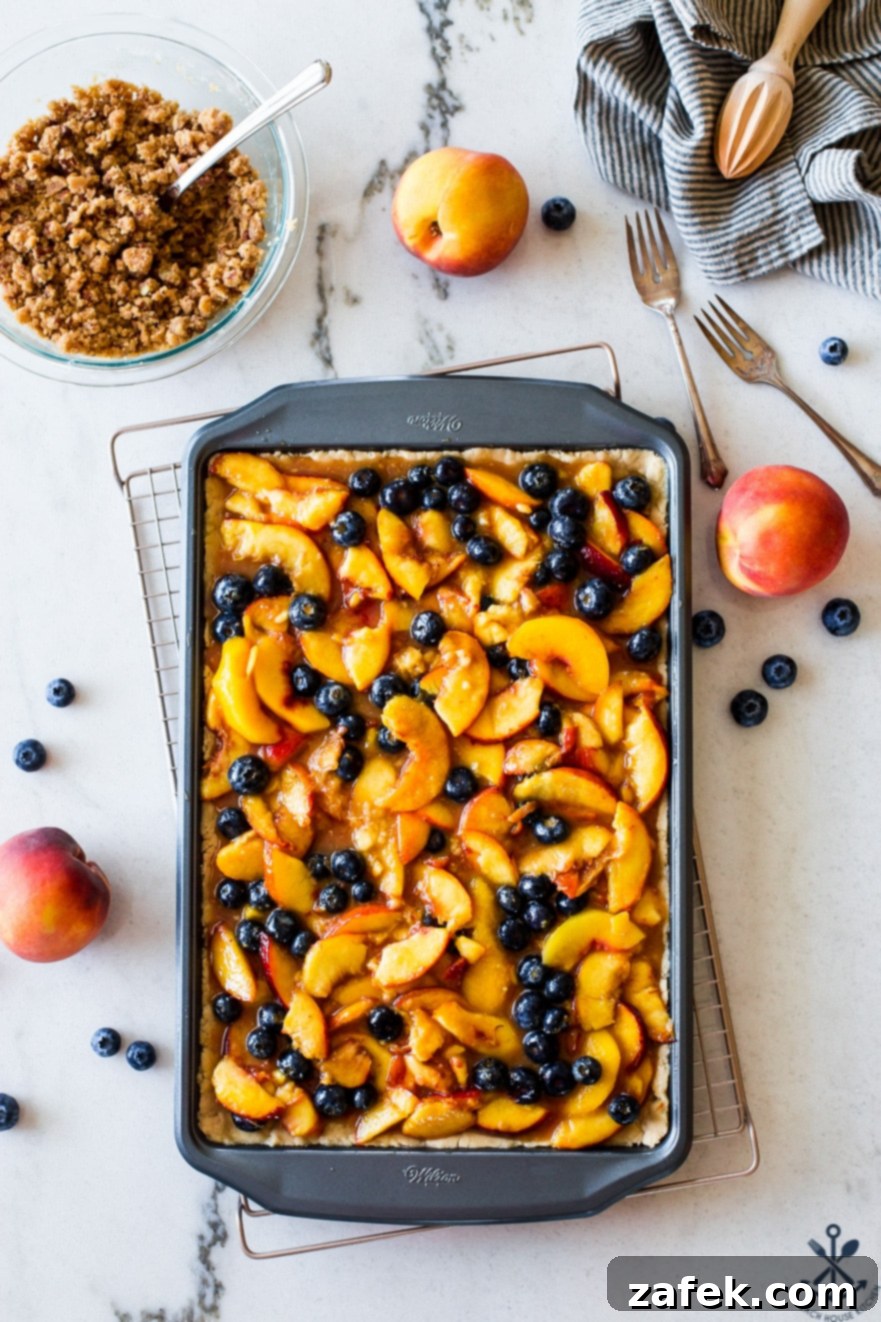 Sweet Summer Peach Blueberry Crumble Slab 3 Overhead photo of a sheet pan generously filled with fresh, vibrant peaches and blueberries, ready for baking.