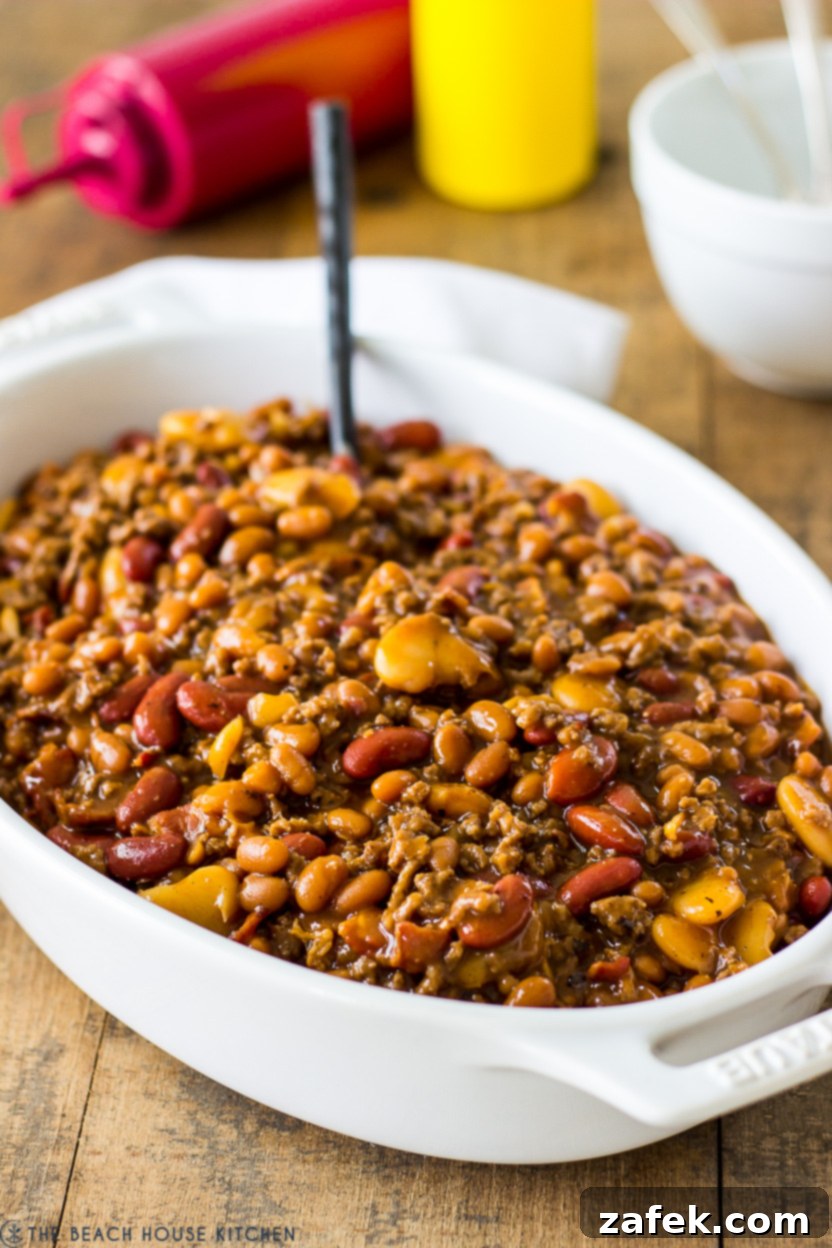 Hearty Three-Bean Casserole 2 A baked three bean casserole in a white oval dish, rich with beans, ground beef, and a savory sauce.