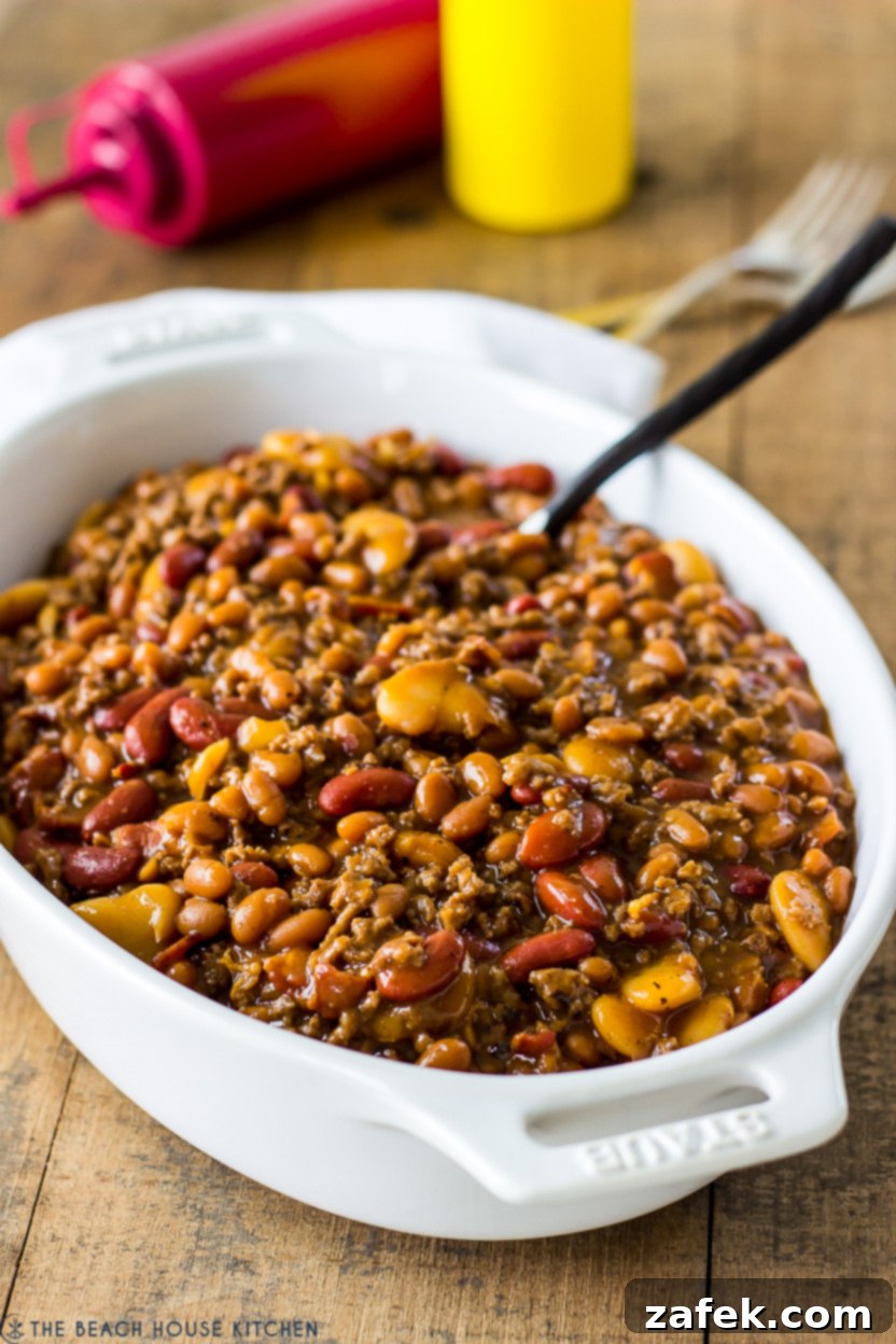 Hearty Three-Bean Casserole 3 A baked three bean casserole in a white oval dish on a rustic wooden surface, ready to be served.