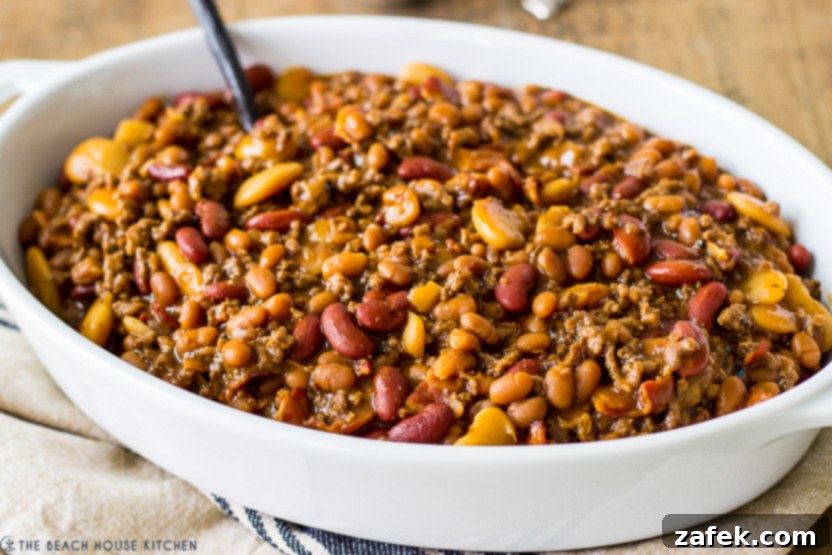 Hearty Three-Bean Casserole 4 Up close photo of a bean casserole in a white baking dish, showing the rich, bubbly topping.