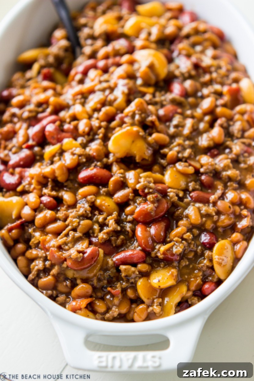 Hearty Three-Bean Casserole 6 A baked bean casserole in a white oval baking dish, golden brown and bubbling.