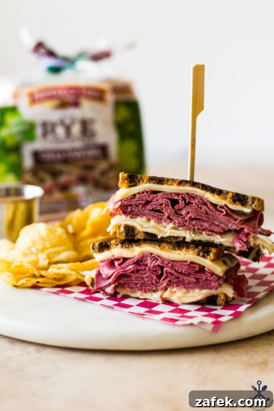 A perfectly grilled Classic Reuben Sandwich, cut in half, revealing layers of corned beef, Swiss cheese, and sauerkraut. Served with a side of crispy potato chips, with a loaf of rye bread visible in the soft-focus background.
