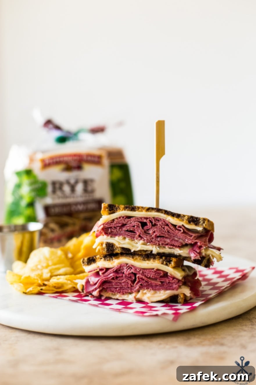 A close-up of a grilled Reuben sandwich, cut in half, accompanied by golden potato chips. In the background, a new package of deli swirl rye bread awaits its turn.