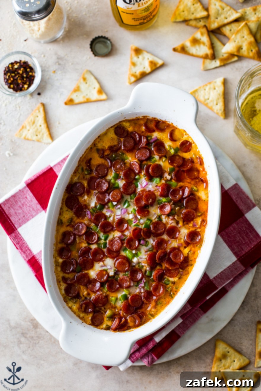 Overhead photo of a white oval dish filled with baked pepperoni dip and crackers around