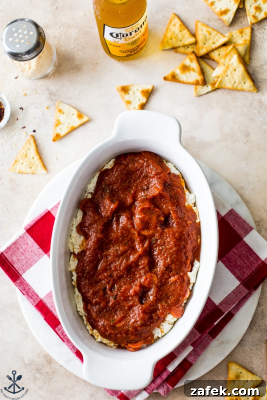 Overhead photo of a the white oval dish filled with cream cheese mixture topped with pizza sauce