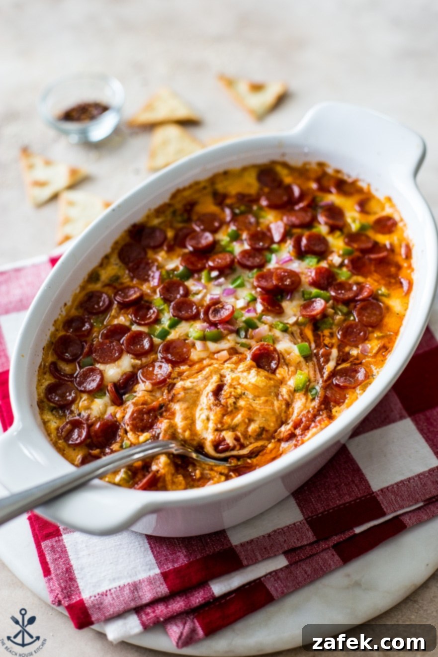 Cheesy Pepperoni Dip in a white oval dish with a spoon on a red checked napkin