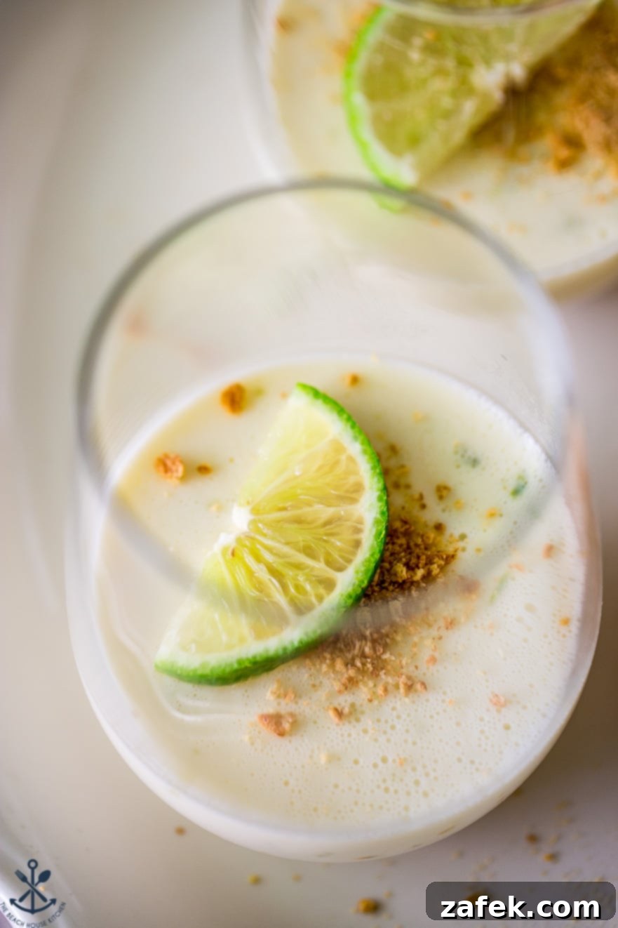 Zesty Key Lime Panna Cotta 5 Up close photo of a glass filled with panna cotta, a lime slice and graham cracker crumbs