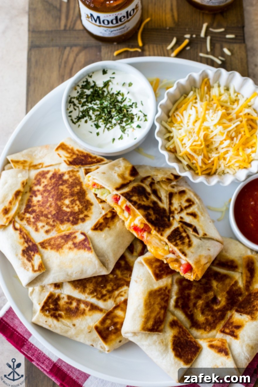 Buffalo Chicken Ultimate Crispy Wraps 3 An overhead shot of two homemade Buffalo Chicken Crunchwrap Supremes on a pristine white platter, garnished with a sprinkle of shredded cheese and a dollop of creamy sour cream, ready to be enjoyed.