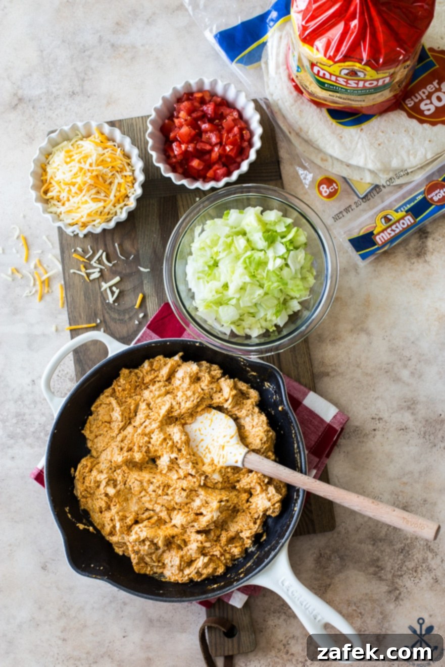Buffalo Chicken Ultimate Crispy Wraps 6 A comprehensive overhead flat lay of all ingredients for Buffalo Chicken Crunchwrap Supremes, including chicken, sauces, cheeses, fresh produce, tortillas, and a skillet, arranged on a wooden board.
