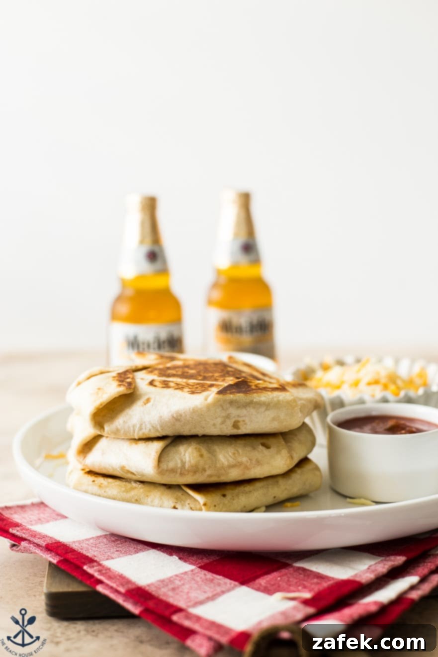 Buffalo Chicken Ultimate Crispy Wraps 8 A stack of golden-brown crunchwraps rests on a white platter, flanked by two blurred glasses of beer in the background, evoking a casual and celebratory meal scene.