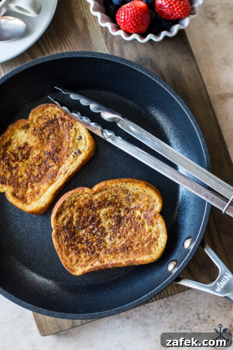 Aromatic Chai French Toast 3 Overhead photo of a skillet with two slices of french toast and a set of silver tongs