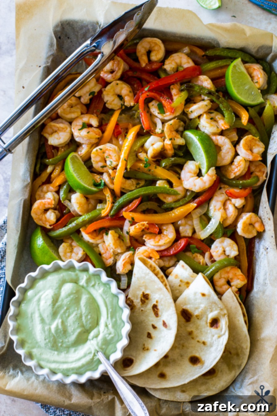 Effortless Sheet Pan Shrimp Fajitas 2 Overhead photo of shrimp and veggies on baking sheet with avocado creama