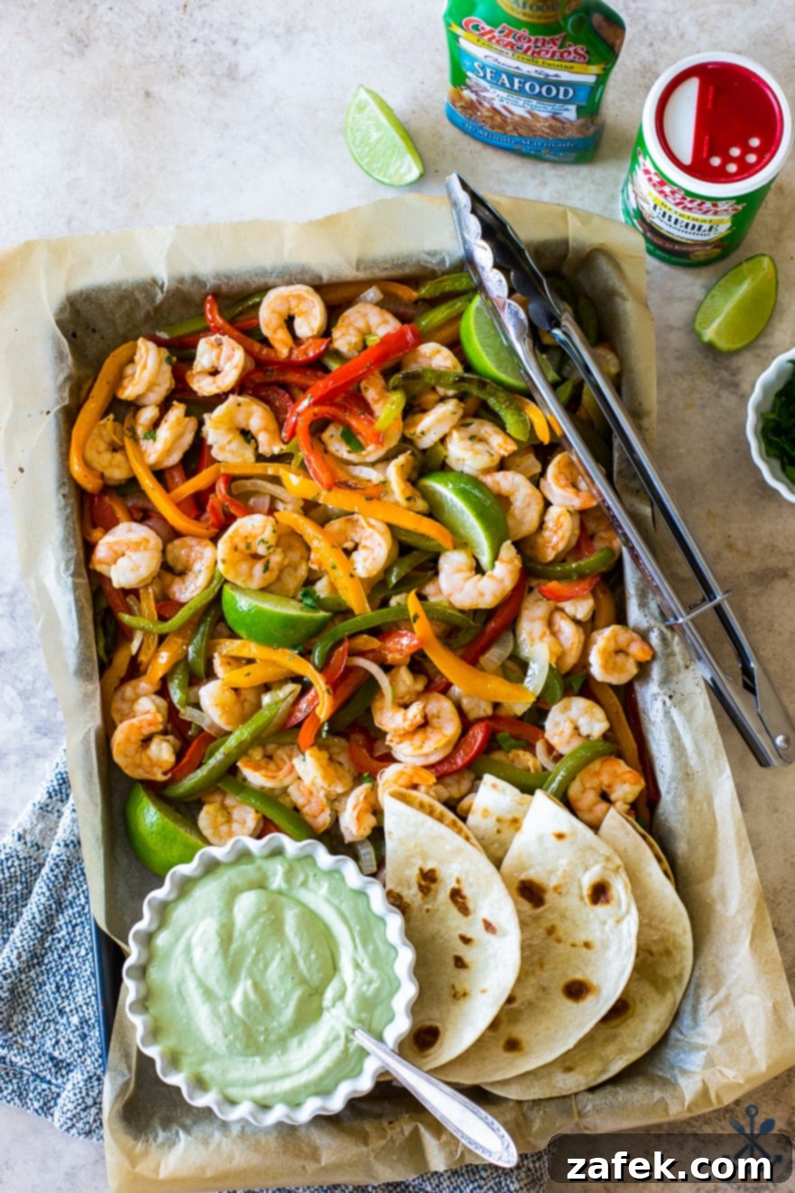 Effortless Sheet Pan Shrimp Fajitas 3 Overhead photo of a sheet pan filled with shrimp and onions and peppers and a bowl of avocado crema