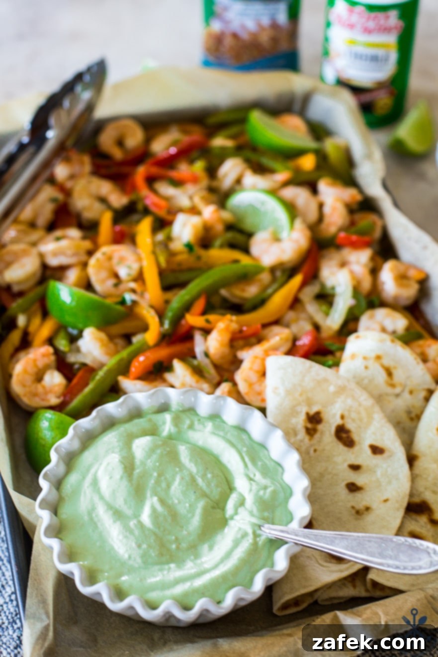 Effortless Sheet Pan Shrimp Fajitas 7 Up close photo of a bowl of avocado crema with shrimp, onions, peppers and tortillas in bacjground