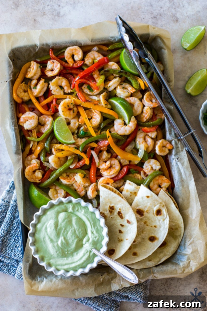 Effortless Sheet Pan Shrimp Fajitas 10 Overhead photo of a large sheet pan with shrimp, peppers, onions and a bowl of avocado crema