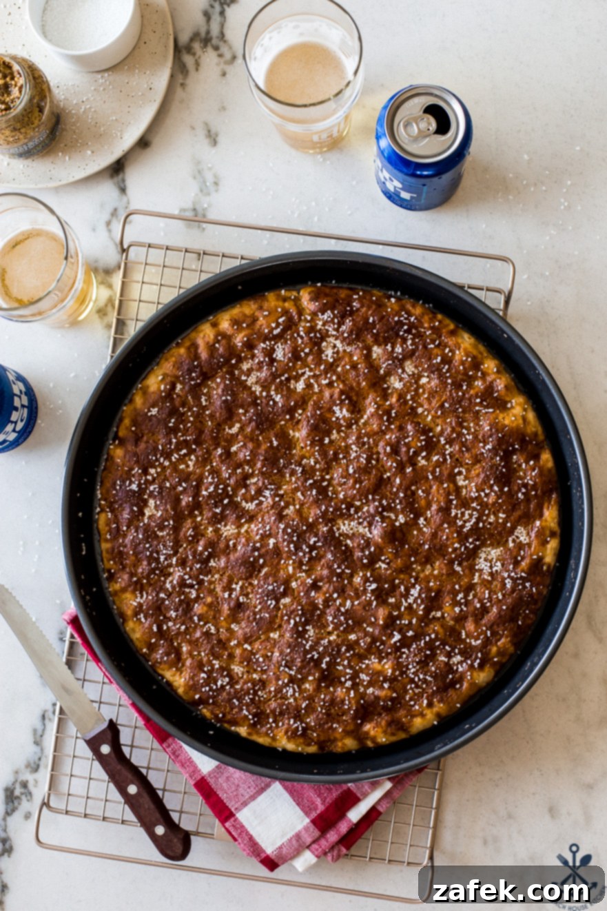 Overhead photo of pretzel focaccia in a round baking pan on a wire rack.