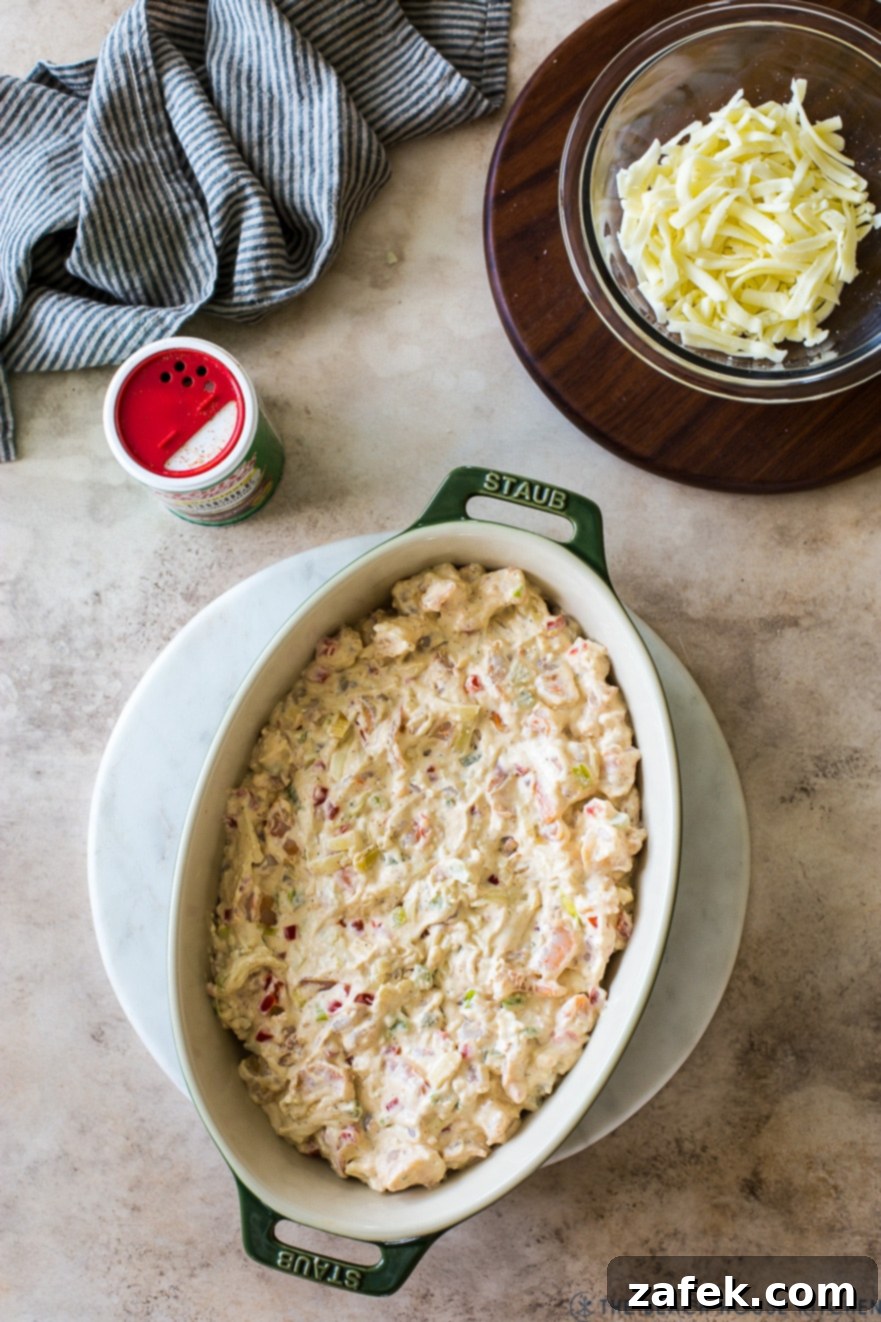 Creole Shrimp Kick 5 Overhead photo of an oval baking dish filled with pre-baked shrimp dip, ready for the oven with cheese sprinkled on top.