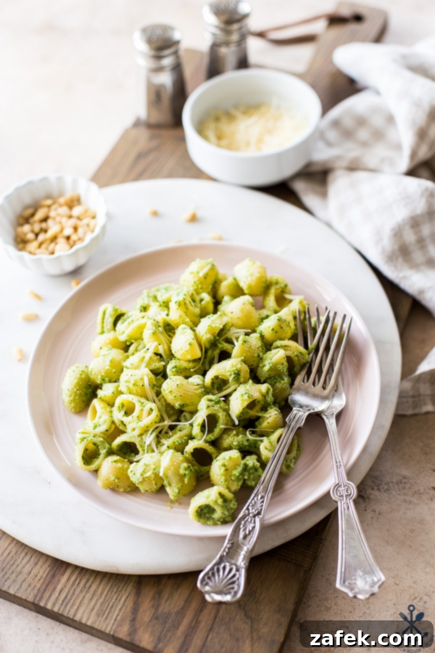 A light pink dish of pesto pasta with two forks, garnished with fresh basil leaves