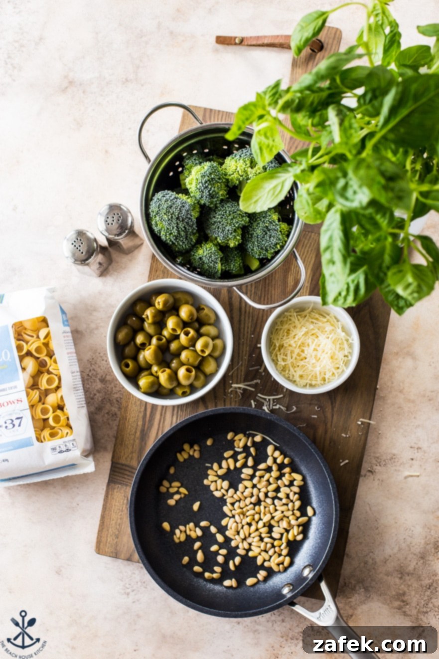 Overhead photo of ingredients for pesto pasta laid out: fresh broccoli florets, pine nuts, pitted green olives, and fragrant basil leaves