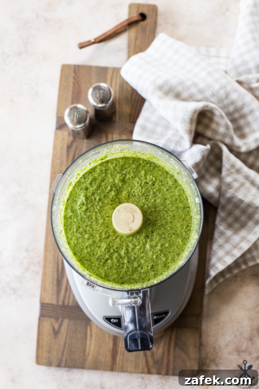 Overhead photo of a food processor bowl filled with smooth, vibrant green broccoli pesto sauce, ready to be used