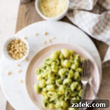 Overhead photo of a pink plate of Broccoli Pesto Pasta on a round marble board with a small bowl of pine nuts