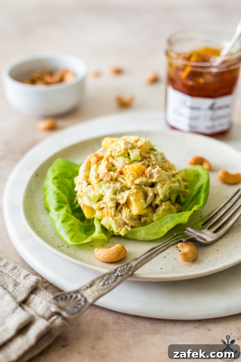 A scoop of curried chicken salad on a piece of lettuce on a plate, garnished with chopped cashews