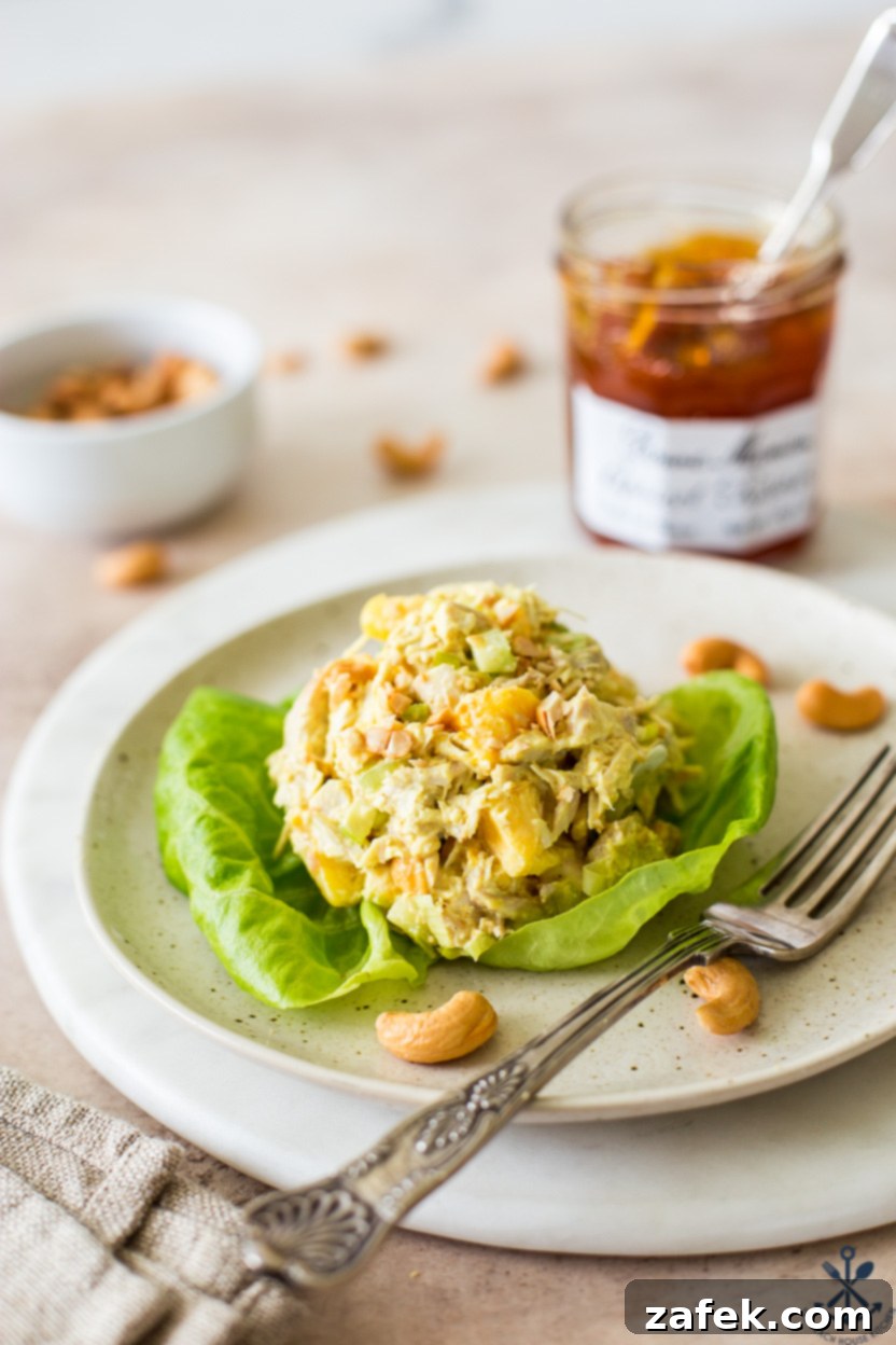 Curried chicken salad on a piece of lettuce on a plate with a fork, with a jar of apricot preserves in the softly blurred background