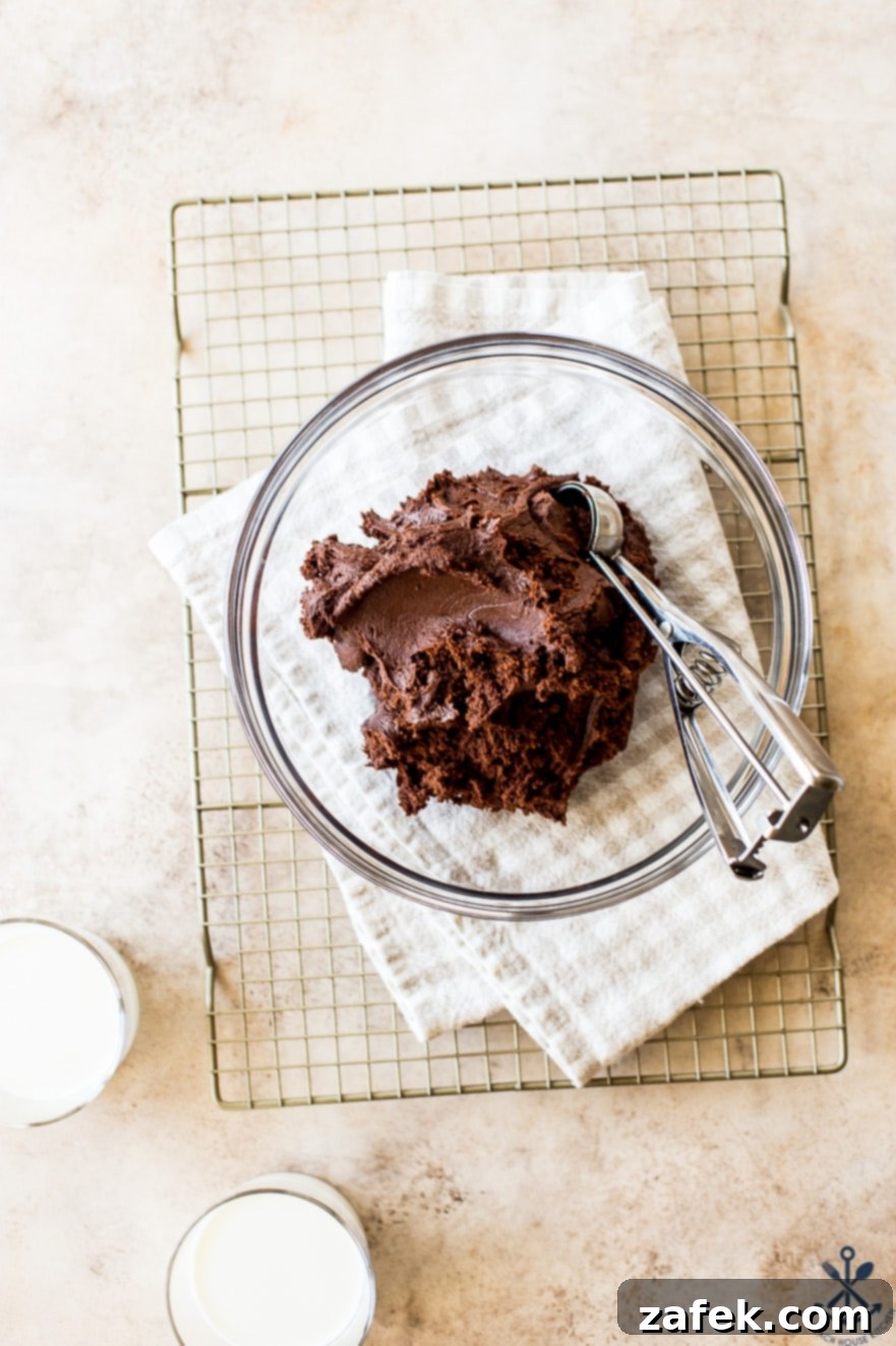 Decadent Fudgy Brownie Cookies 4 A glass bowl filled with brownie cookie dough and a cookie scooper on a wire rack