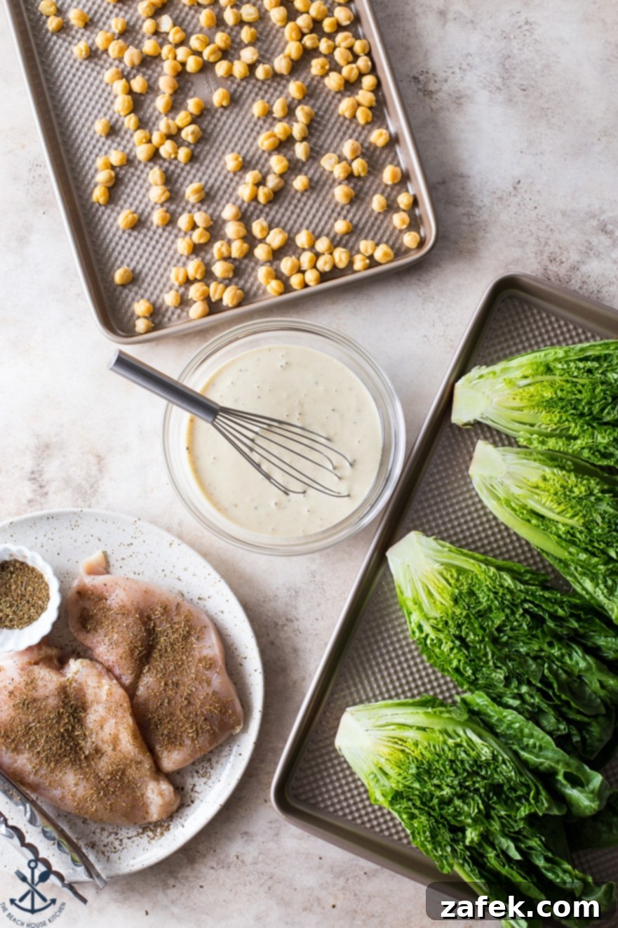 Chargrilled Chicken Caesar with Roasted Chickpea Crunch 5 An array of fresh ingredients for the Grilled Chicken Caesar Salad: a sheet pan of golden roasted chickpeas, a bowl of homemade Caesar dressing with a whisk, a plate of seasoned chicken breasts ready for grilling, and a sheet pan with halved heads of romaine lettuce prepared for grilling.