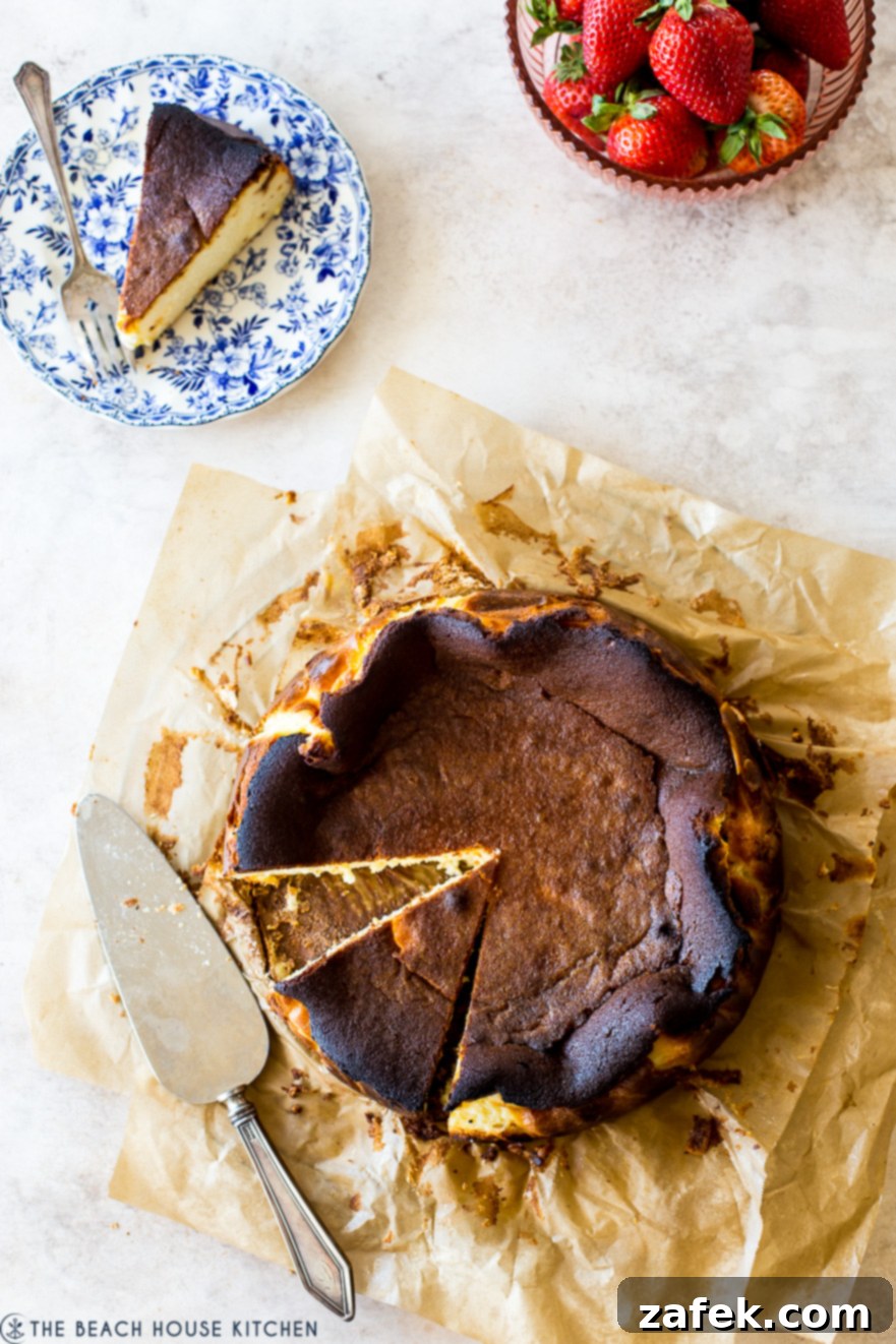 San Sebastian Burnt Cheesecake 2 Overhead photo of Burnt Basque Cheesecake on parchment paper with a bowl of strawberries and a slice on a plate with a fork