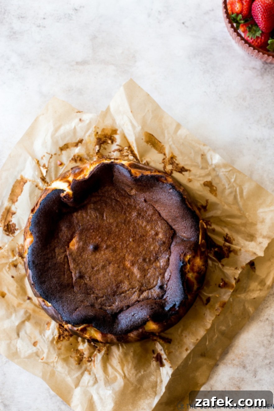 San Sebastian Burnt Cheesecake 6 Overhead photo of a dark cheesecake on parchment paper with a bowl of strawberries off to the top right corner