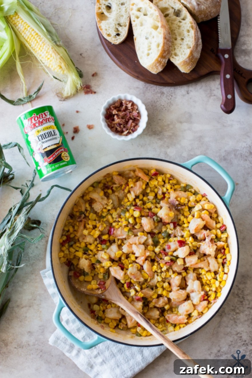Overhead photo of a baking dish with vibrant shrimp maque choux and a wooden spoon, ready to be served.
