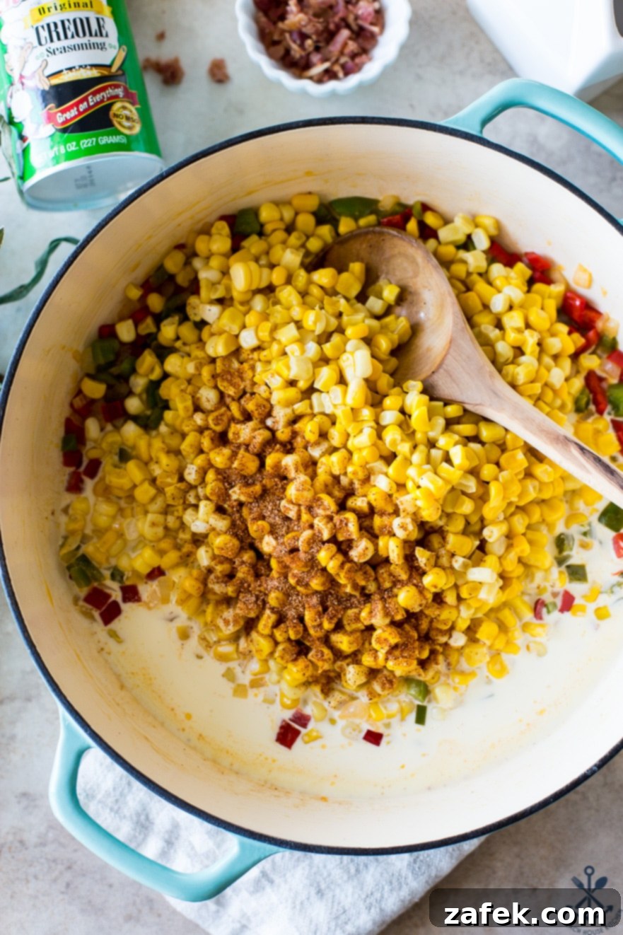 Up close overhead photo of fresh corn kernels, chopped bell peppers, onions, and heavy cream in a baking dish with a wooden spoon, showcasing the ingredients before simmering.