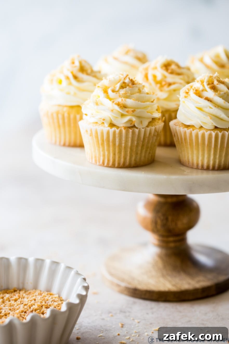 Beautifully decorated Piña Colada Cupcakes on a tiered cake stand, garnished with toasted coconut flakes, ready to be enjoyed.