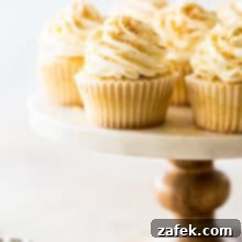 Beautifully frosted Piña Colada Cupcakes, adorned with toasted coconut, showcased on a wooden cake stand.
