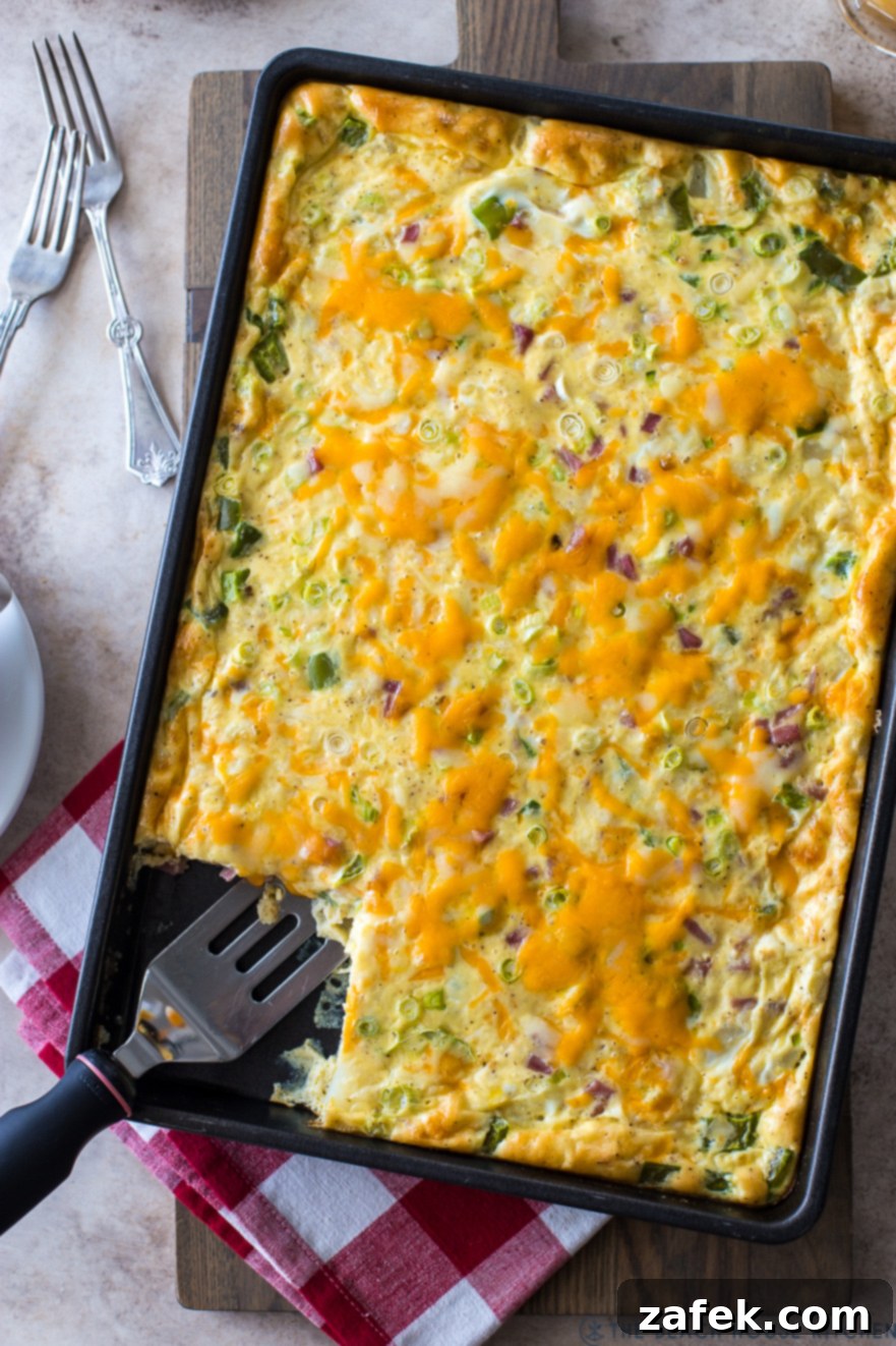 Up close overhead photo of a cooked sheet pan Denver omelette, showcasing the golden-brown edges, melted cheese, and colorful fillings