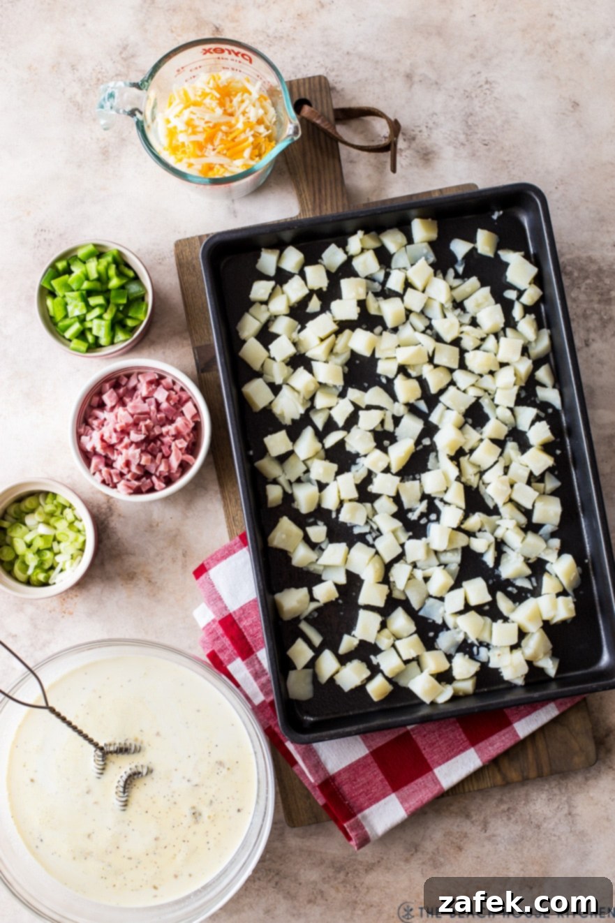 Overhead photo of a sheet pan of cubed potatoes and bowls filled with denver omelette ingredients including diced ham, bell peppers, and cheese