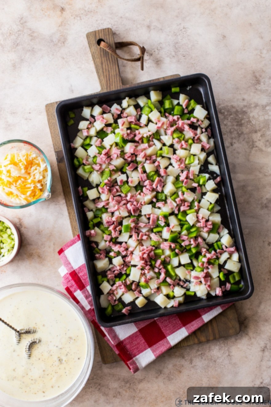 Overhead photo of a sheet pan loaded with pre-baked cubed potatoes, green peppers, and diced ham, ready for the egg mixture
