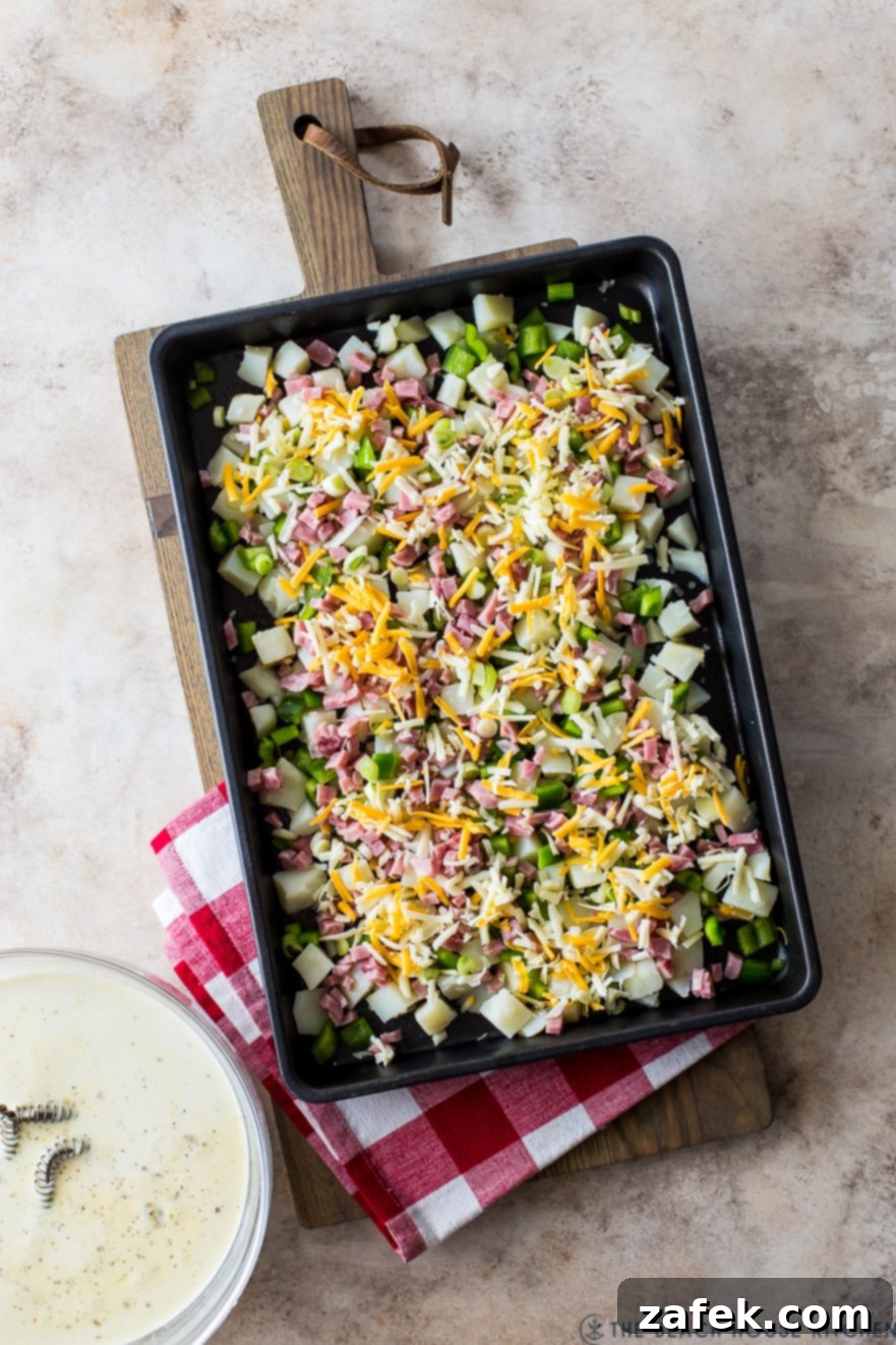 Up close overhead photo of a sheet pan filled with cubed potatoes, green peppers, ham, and shredded cheese, just before baking