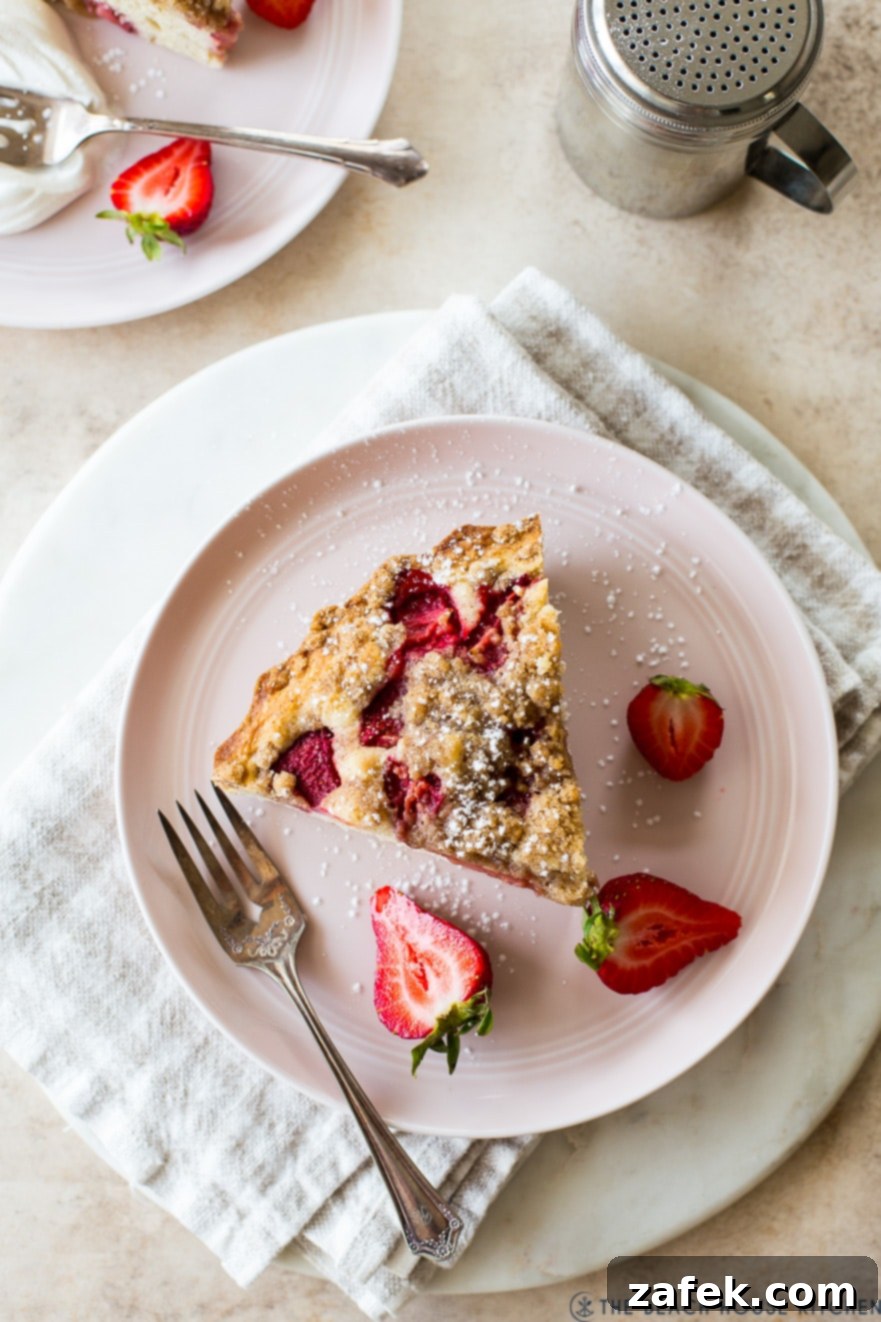 Sweet Strawberry Streusel 5 An inviting overhead view of a single serving of Strawberry Buckle on a charming pink plate, garnished with additional fresh strawberry slices, a fork resting beside it, highlighting the dessert's irresistible appeal.