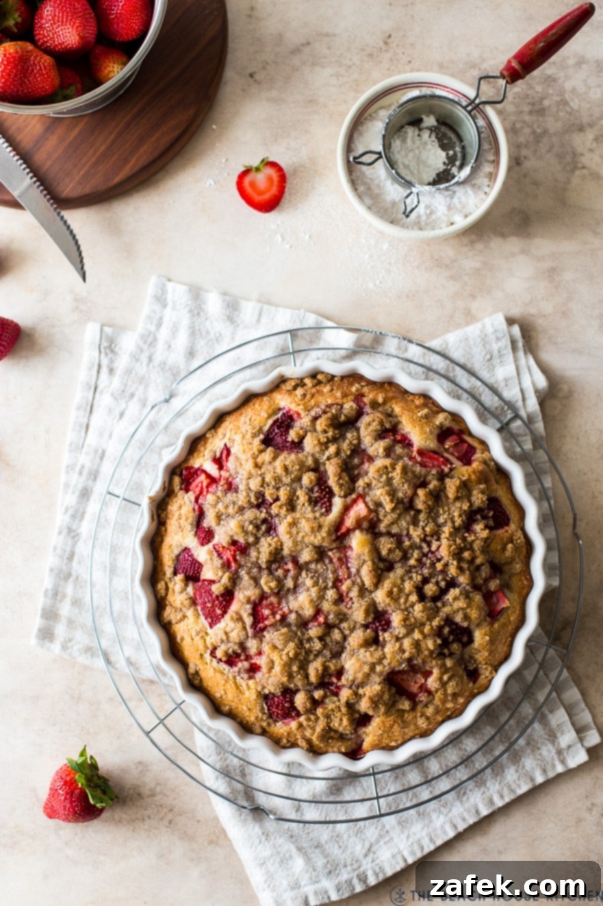 Sweet Strawberry Streusel 9 An aerial view of the finished Strawberry Buckle, adorned with its baked strawberries and streusel, cooling gracefully on a wire rack atop a light brown and white checked napkin, embodying rustic charm.