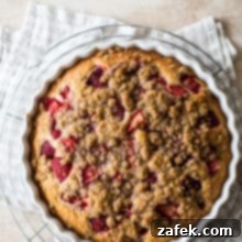 Sweet Strawberry Streusel 10 A beautiful Strawberry Buckle with a golden crumb topping and visible strawberries, captured up close in a white round baking dish, set against a warm-toned checked napkin, perfect for a summer dessert.