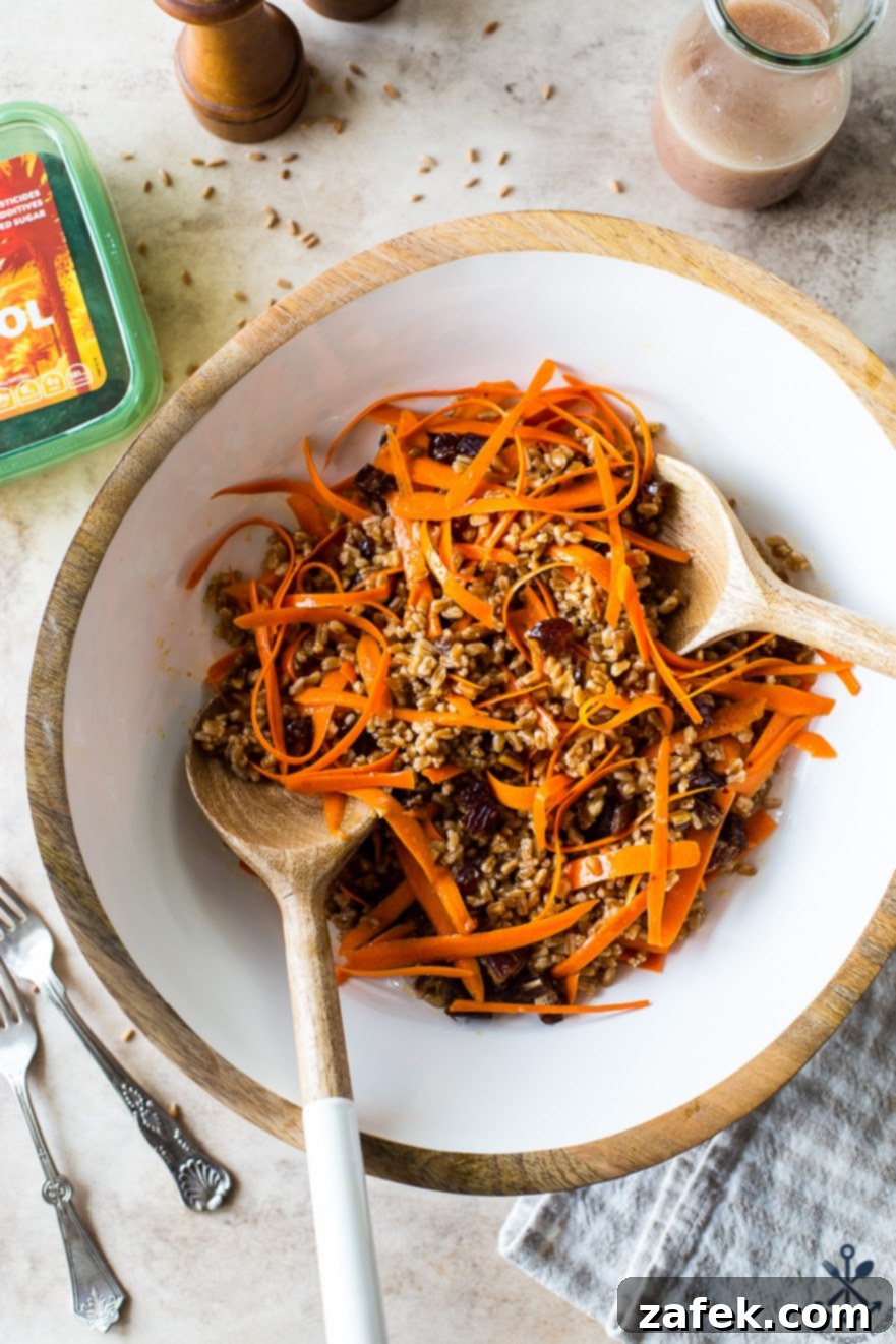 Farro and Carrot Salad with Maple-Date Vinaigrette 2 Overhead photo of a healthy Carrot Farro Salad with Dates and Maple Vinaigrette, beautifully presented in a white bowl with serving utensils, highlighting its rich colors and textures.