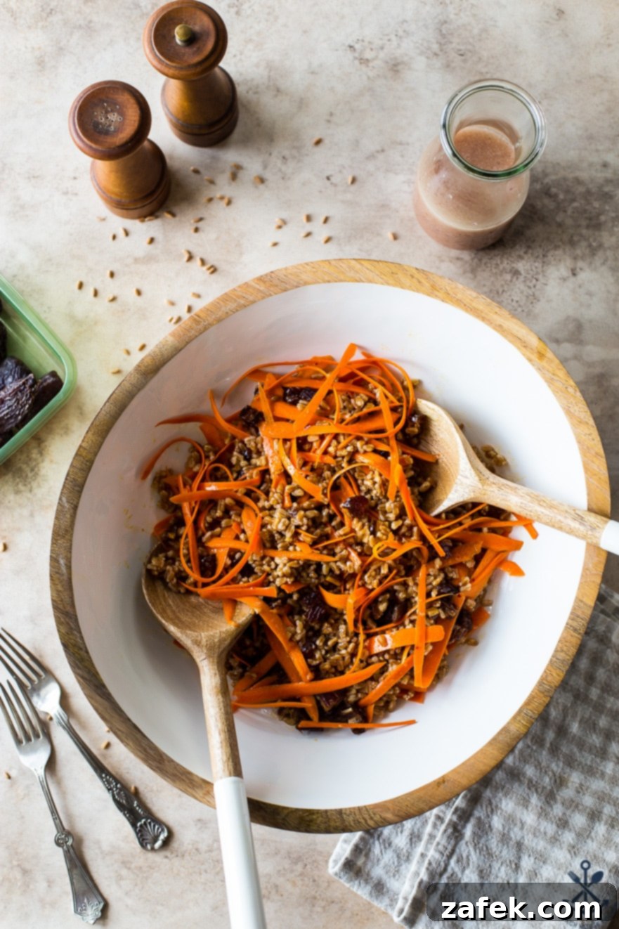 Farro and Carrot Salad with Maple-Date Vinaigrette 3 Overhead photo showcasing a prepared Carrot Farro Salad with Dates and Maple Vinaigrette in a elegant white bowl, accompanied by a bottle of the homemade dressing and salt and pepper shakers, creating a rustic yet refined dining scene.